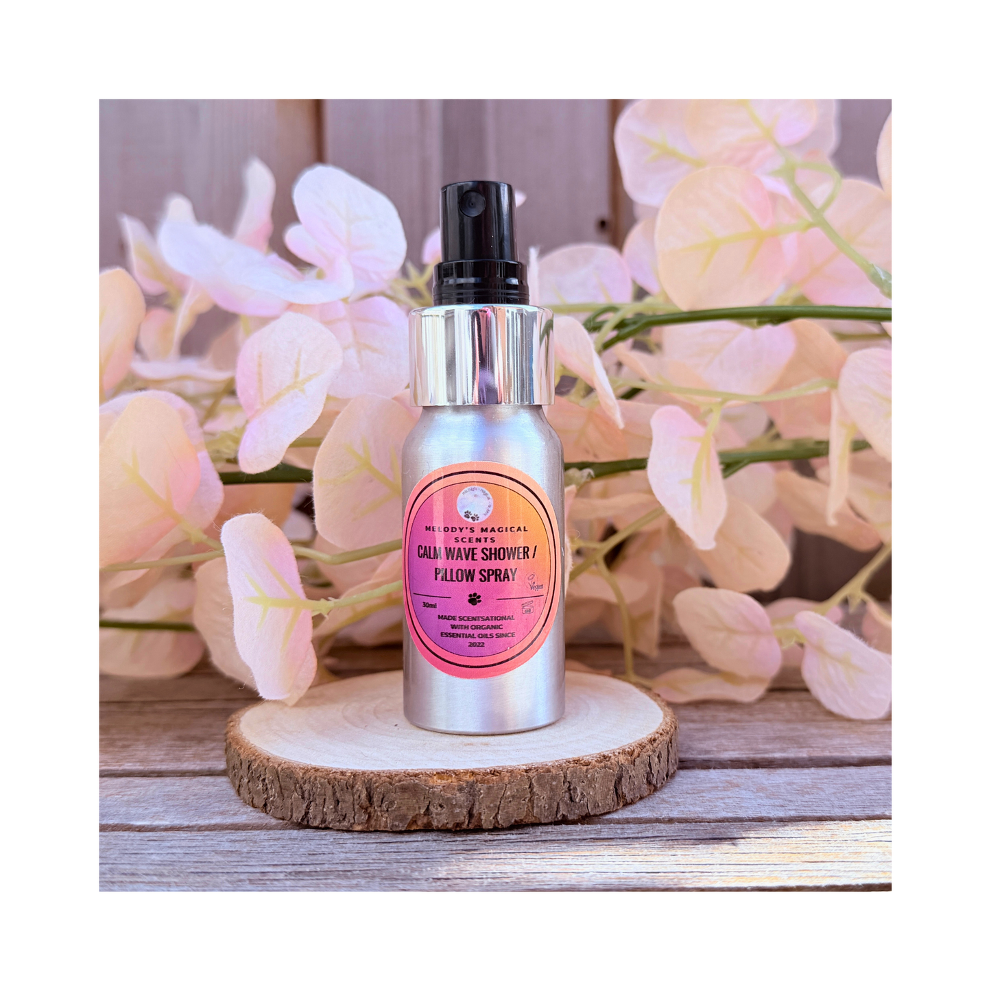 Silver bottle with pink label on a wooden coaster with flowers in the background