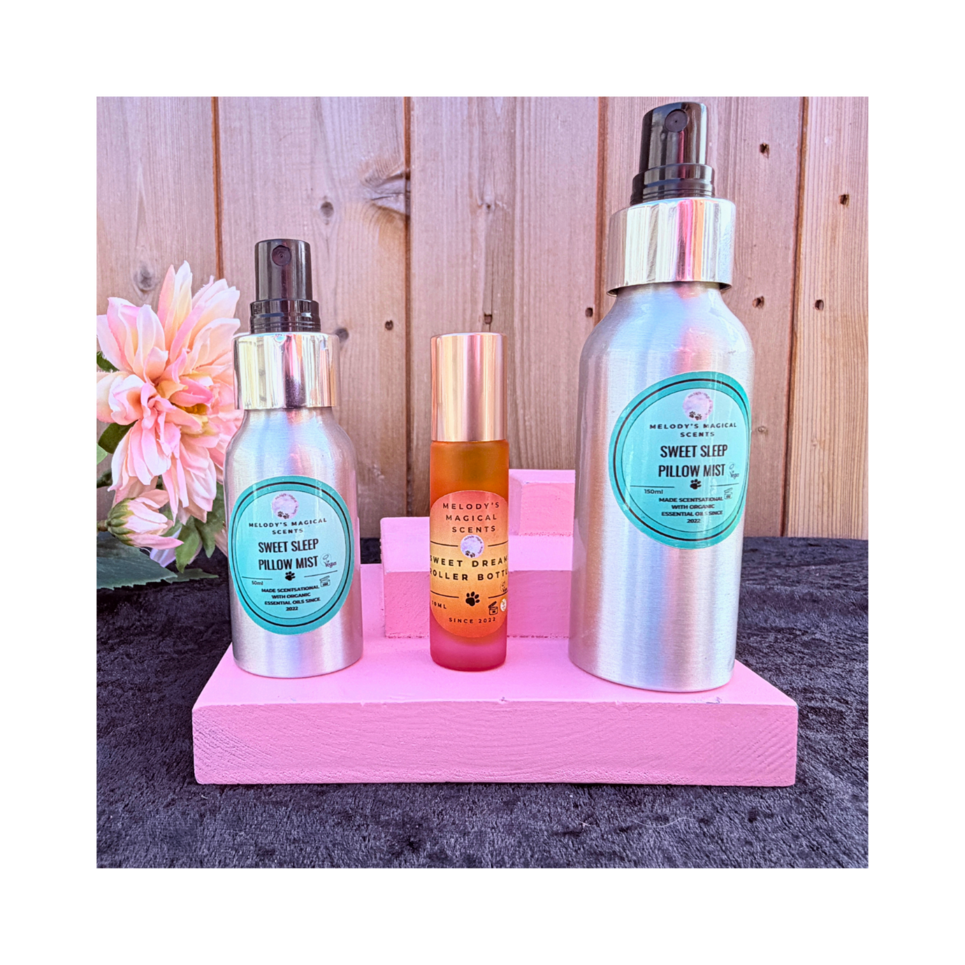 Two bottles of 'Sweet Sleep' pillow mist and "Sweet Dreams" roller bottle on a pink stand with a wooden background.
